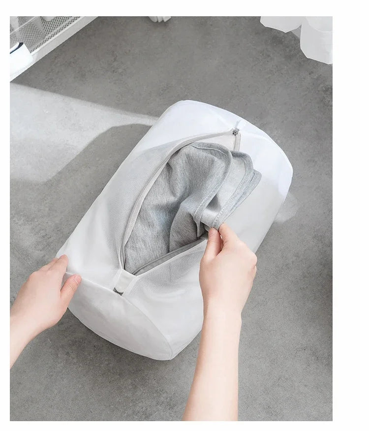 Una mano abre una bolsa de ropa reutilizable de malla blanca para revelar ropa gris dentro.