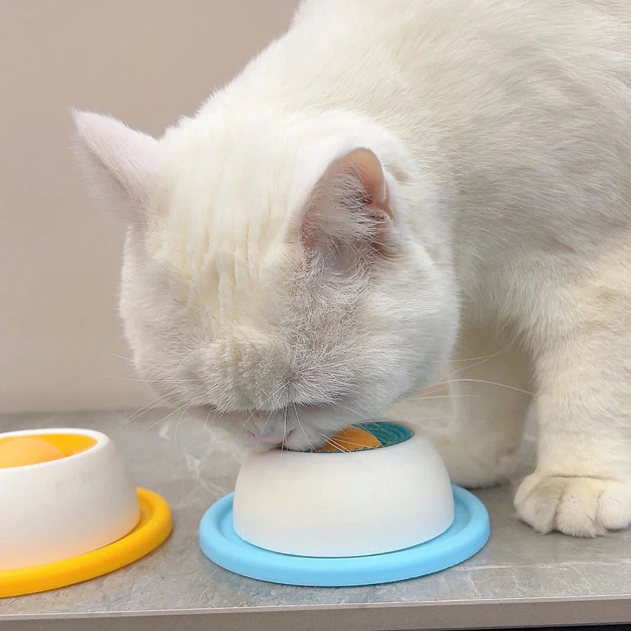 Eine weiße Katze leckt ein interaktives Leckspielzeug für Hunde und Katzen auf einer hellen Oberfläche.