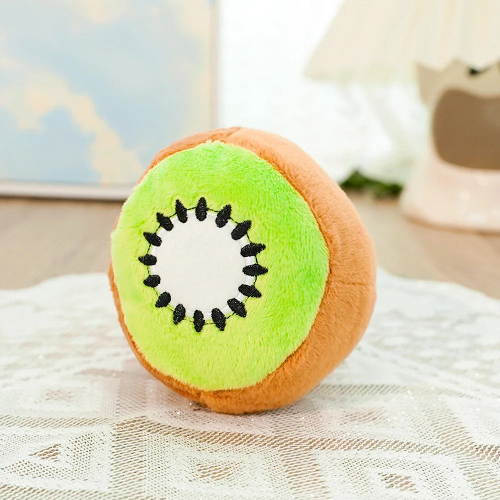 A plush toy shaped like an avocado with a kiwi pattern on the skin, resting on a white lace surface.