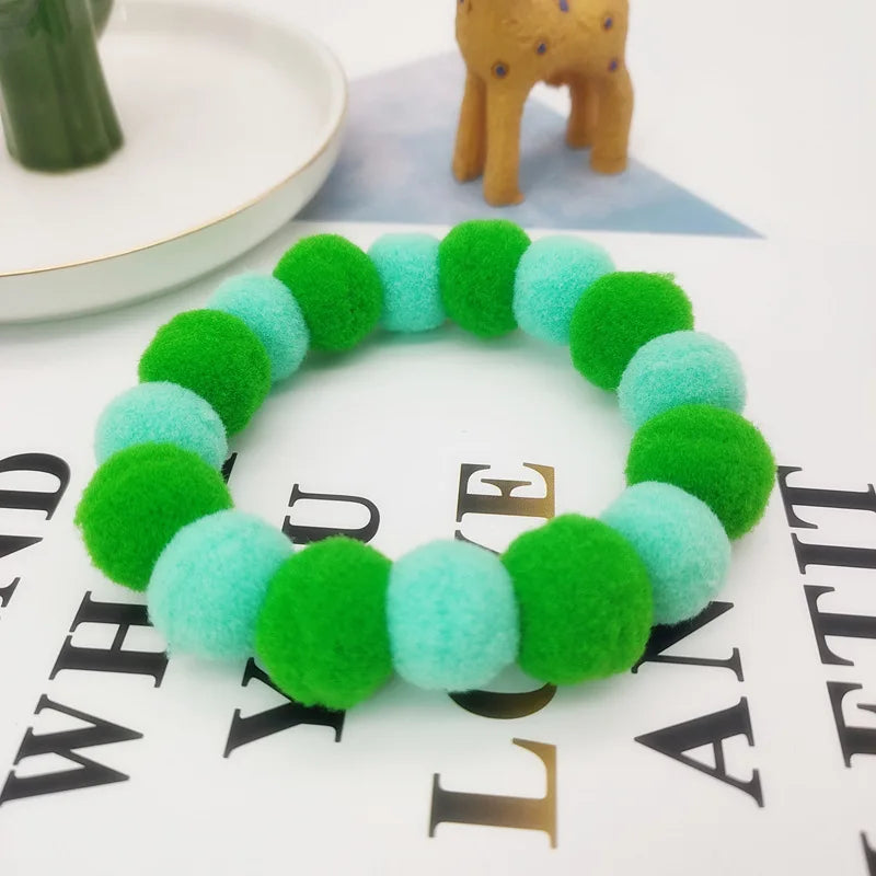 A green and light blue fuzzy collar made of felt is displayed on a white background next to a small stuffed elephant.