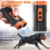 A hand holds an orange ultrasonic dog repellent device, with a dog running in the background.