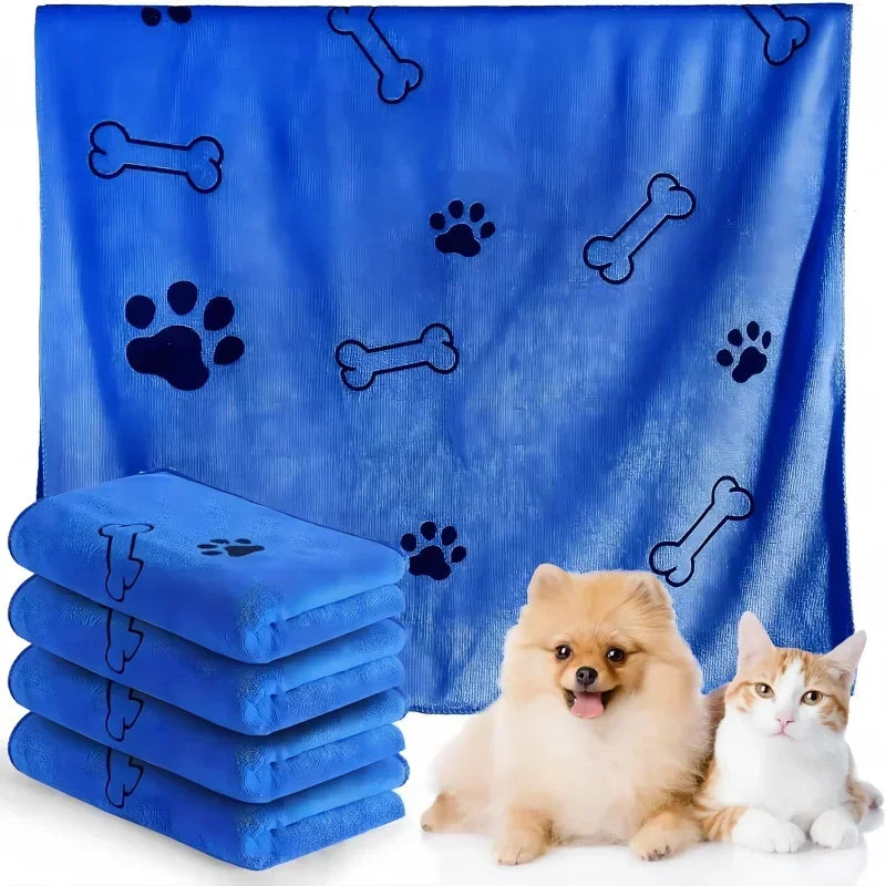 A bright blue ultra-soft quick-dry pet bath towel featuring paw print and bone patterns, with stacked towels and a small dog 