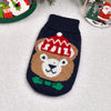 A knitted dog sweater featuring a brown bear face with a red hat and green collar, displayed on a white fuzzy surface.