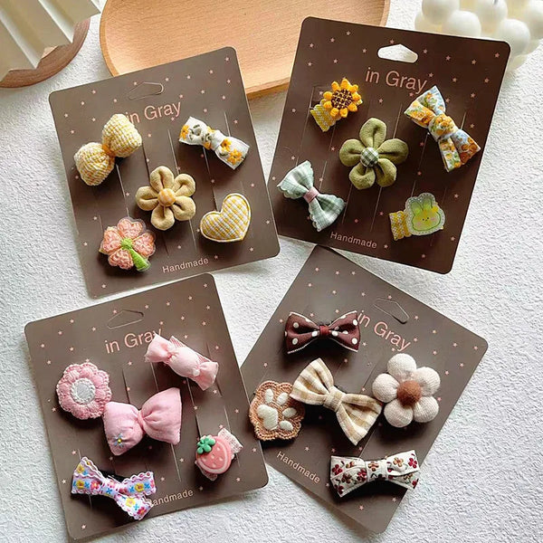 A collection of five handmade fashion pet bows in various colors and textures packaged in brown cardboard holders.