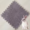 A small gray rabbit sitting on a textured gray fleece pet warming mat.