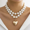 A close-up of a pearl choker necklace with a gold heart pendant worn around the neck.