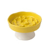 Bol en céramique jaune à nourriture lente pour animaux, posé sur une base blanche.