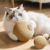 A fluffy white cat is interacting with a natural woven sisal scratching ball on a wooden floor.
