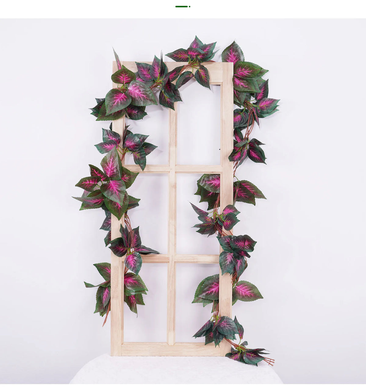 Künstlicher Blätterrank-Girlande mit dunkelgrünen Blättern mit rosa und burgunderfarbener Verfärbung in einem Holzrahmen.