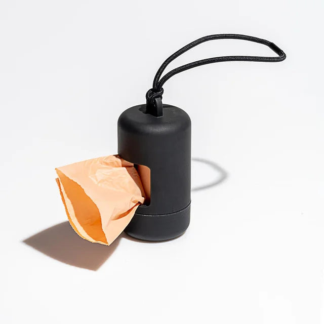 A black portable dog poop bag dispenser with a cardboard bag attached and a black loop for carrying.