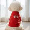 A white dog wearing a red sleeveless vest with a cartoon embroidery on its back.
