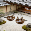 A retro wood grain bird feeder with a hanging iron chain is suspended above a gravel path in a traditional Japanese-style gar