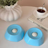 A light blue interactive slow feeder dog bowl resting on a white surface next to a potted plant and a book.