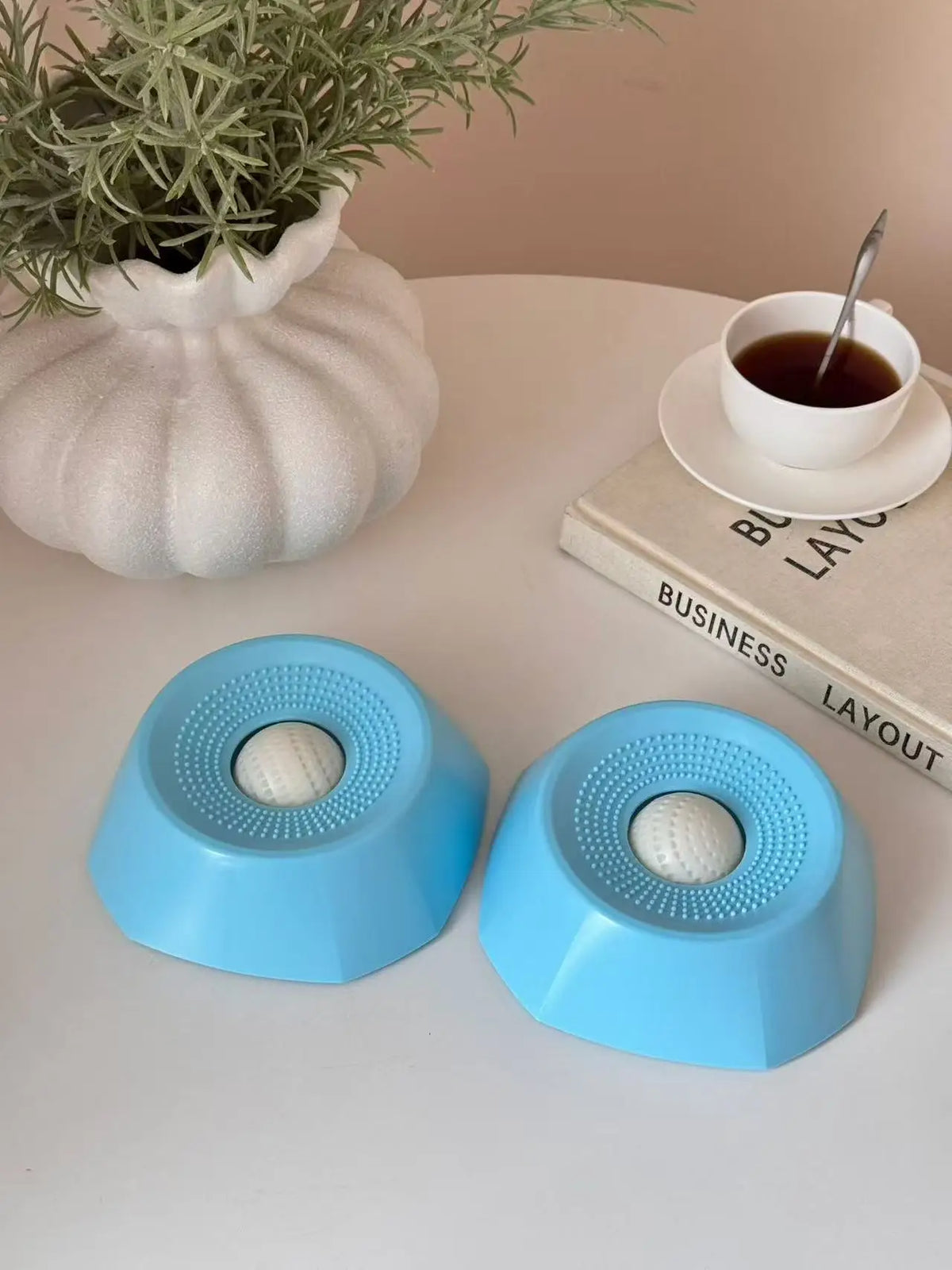 A light blue interactive slow feeder dog bowl resting on a white surface next to a potted plant and a book.