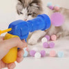 Eine Katze spielt mit einer blauen interaktiven Plüschgewehr und bunten Pompons.