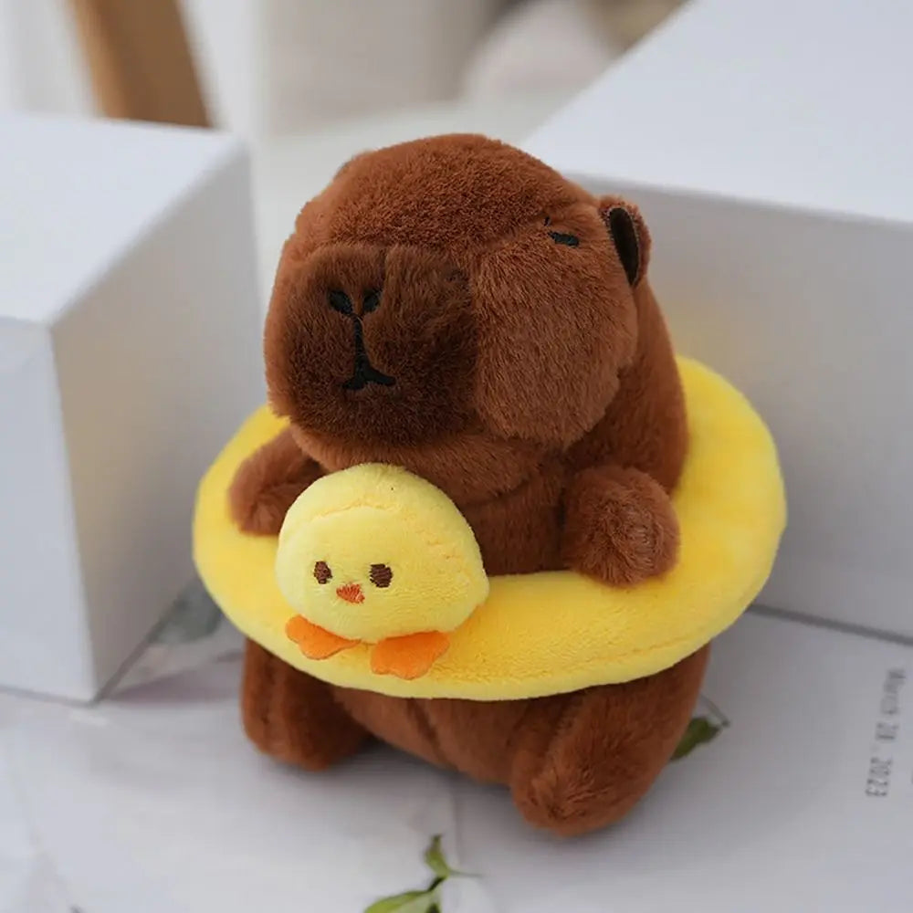 A brown capybara plush toy with a yellow hoodie and a small yellow chick attached, resting on a white box.