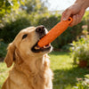 A golden retriever dog is licking an orange EVA chew toy held by a person outdoors.