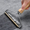 A hand is using a metal lint remover brush with a wooden handle to remove lint from a gray fabric.