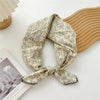 Foulard en coton floral beige clair noué, posé sur un fond en bois.