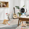 A cat playing with an automatic laser toy on a wooden table, demonstrating interactive play.