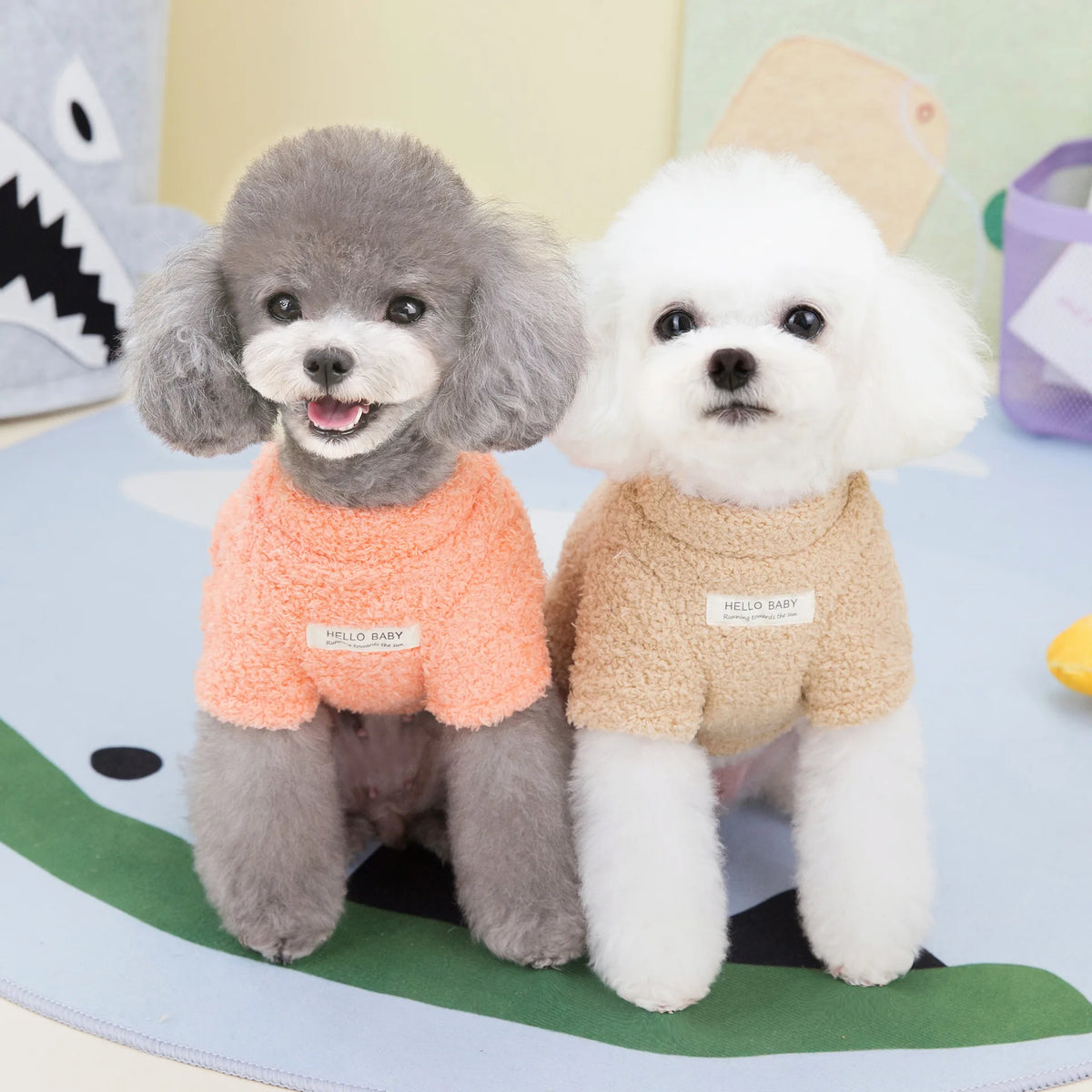 Dos perros pequeños vistiendo abrigadores de invierno de peluche, uno gris y otro blanco, sentados sobre una superficie azul 