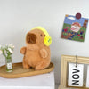 A fluffy brown capybara plush toy sitting on a wooden tray next to a framed picture.