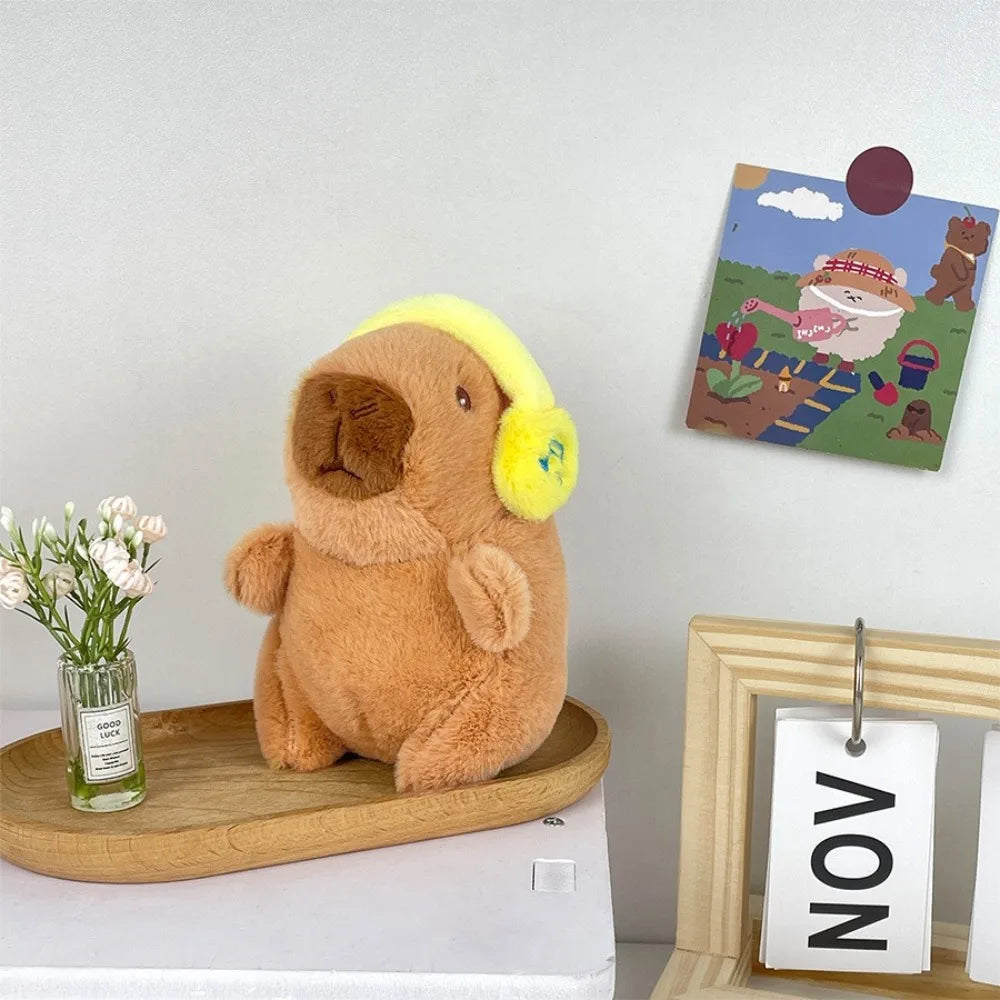 A fluffy brown capybara plush toy sitting on a wooden tray next to a framed picture.