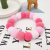 A circular collar made of pink and purple fuzzy material with a small golden elephant toy in the background.