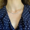 A close-up of a woman wearing a silver snake chain necklace with a heart charm over a dark blue polka dot top.