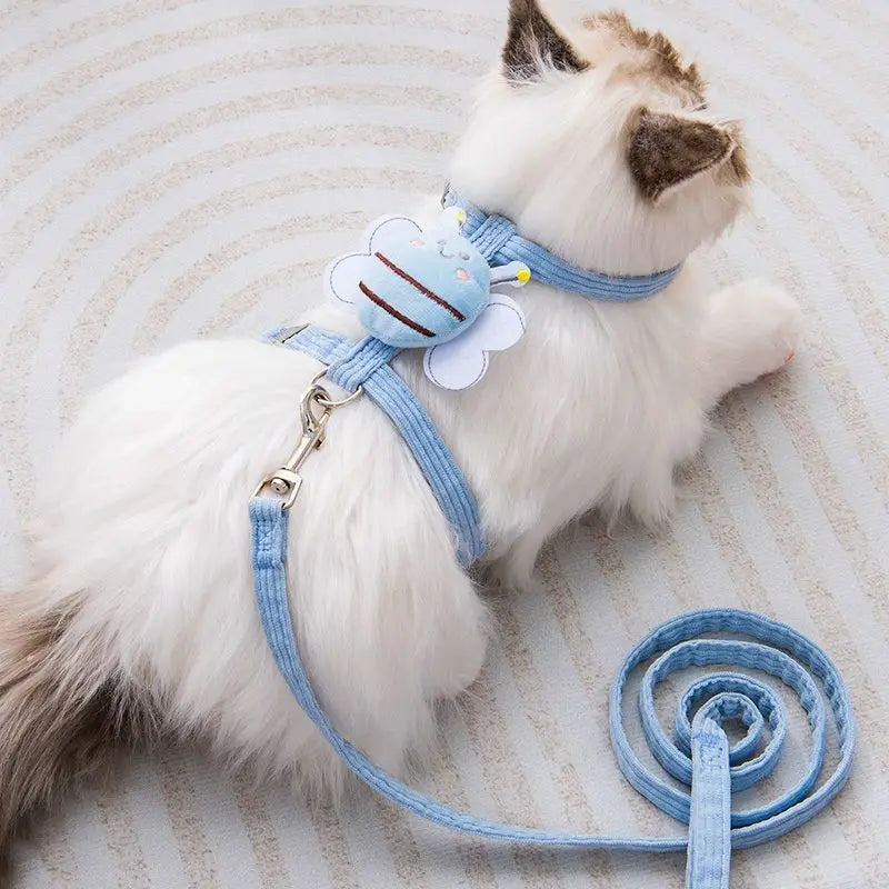 Un gato blanco vistiendo un arnés y correa azul claro ajustable, tumbado sobre un fondo claro.