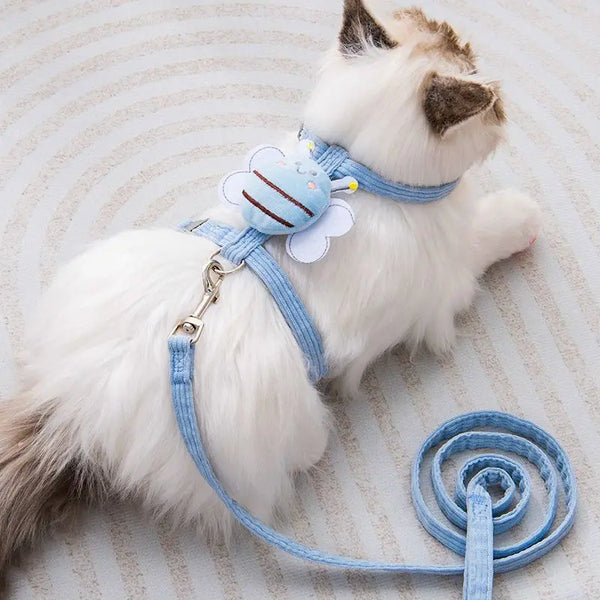 A white cat wearing a light blue adjustable harness and leash lying on a light background.