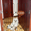 A black metal pet safety gate is installed on a wooden door, featuring a decorative scroll design.