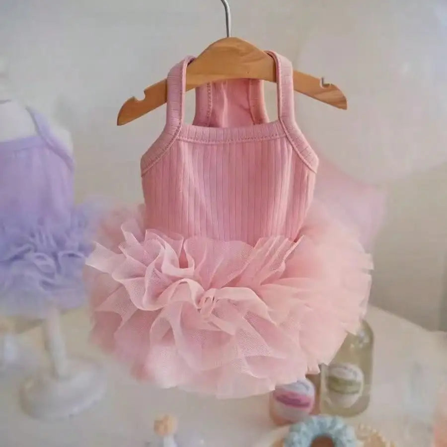 A pink tutu dress for dogs is displayed on a wooden hanger with a fluffy pink tulle skirt.