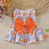 Robe d'été orange et blanc à motifs floraux avec un grand nœud orange, présentée sur un tapis tissé.