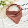 A soft dusty rose triangle scarf is draped on a white surface next to a book.