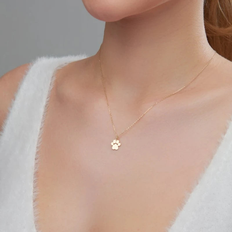 A close-up of a gold-toned cat paw stainless steel pendant necklace worn on a woman's neck.