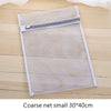 Una bolsa de ropa de malla blanca rectangular con cremallera sobre una superficie de madera.