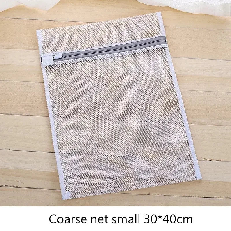 Una bolsa de ropa de malla blanca rectangular con cremallera sobre una superficie de madera.