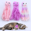 Three plush octopus toys in pink and purple colors next to a sleeping tabby cat.