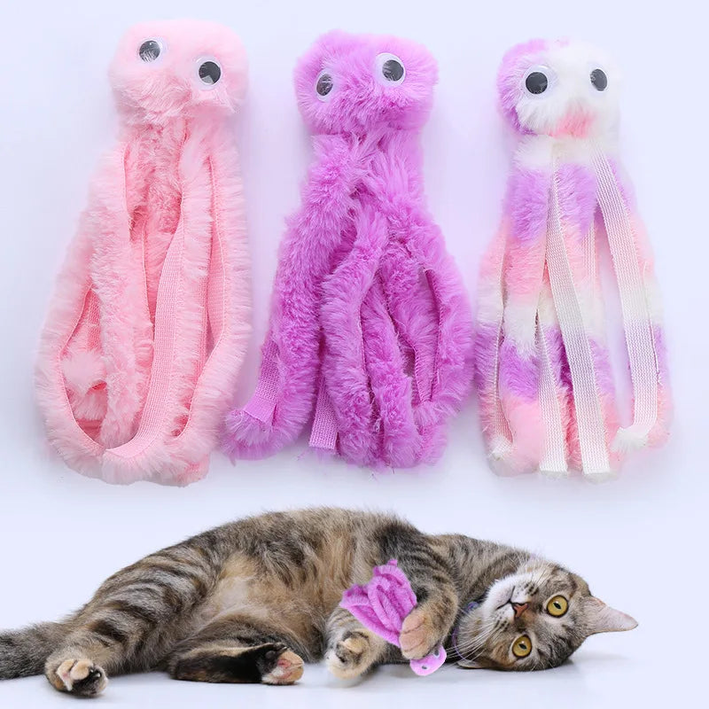 Three plush octopus toys in pink and purple colors next to a sleeping tabby cat.