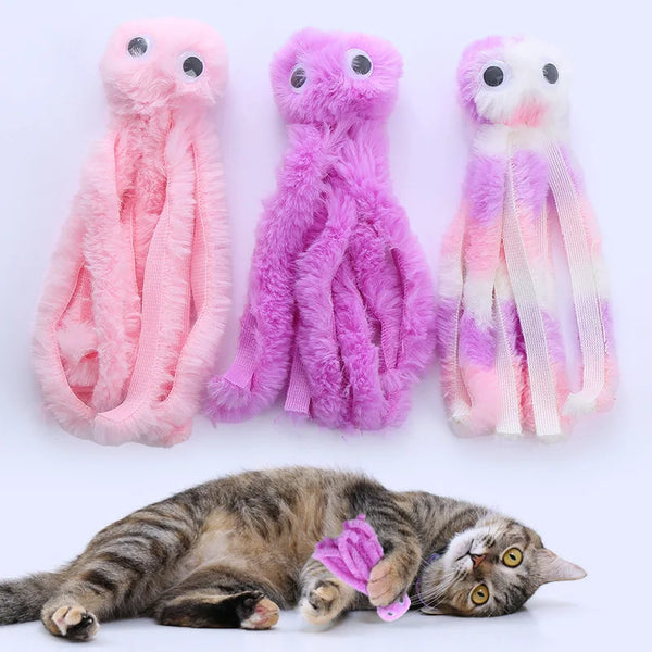 Three plush octopus toys in pink and purple colors next to a sleeping tabby cat.