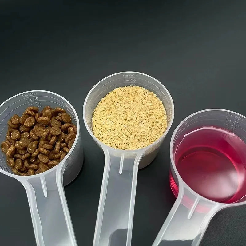 Three transparent measuring spoons hold dog and cat food, including kibble and dry food powder.