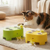 A tabby cat is interacting with a yellow interactive toy featuring a rotating base and feathers on a rug.