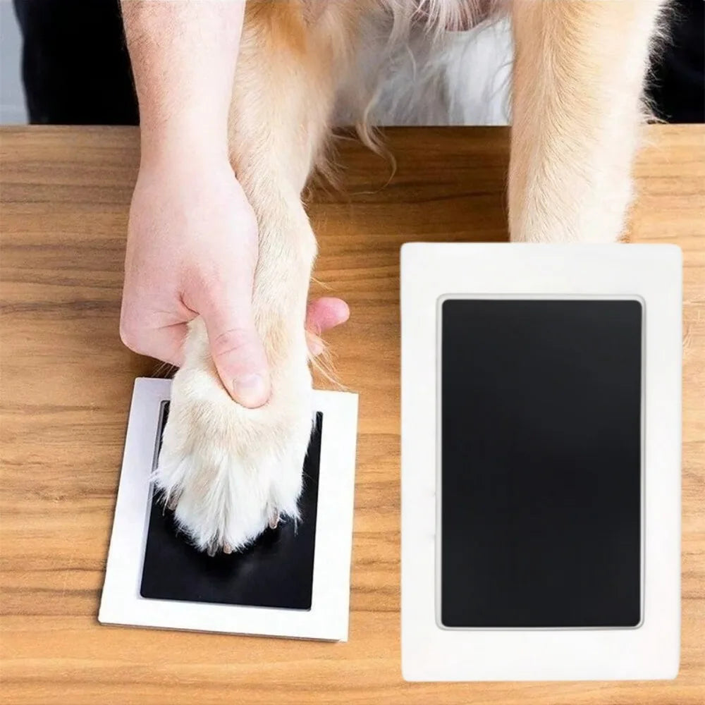 A hand places a paw print on a white plate next to a white digital keepsake kit for pets.