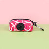 A pink and white patterned stylish dog poop bag holder with a black circular opening is shown on a light green surface.