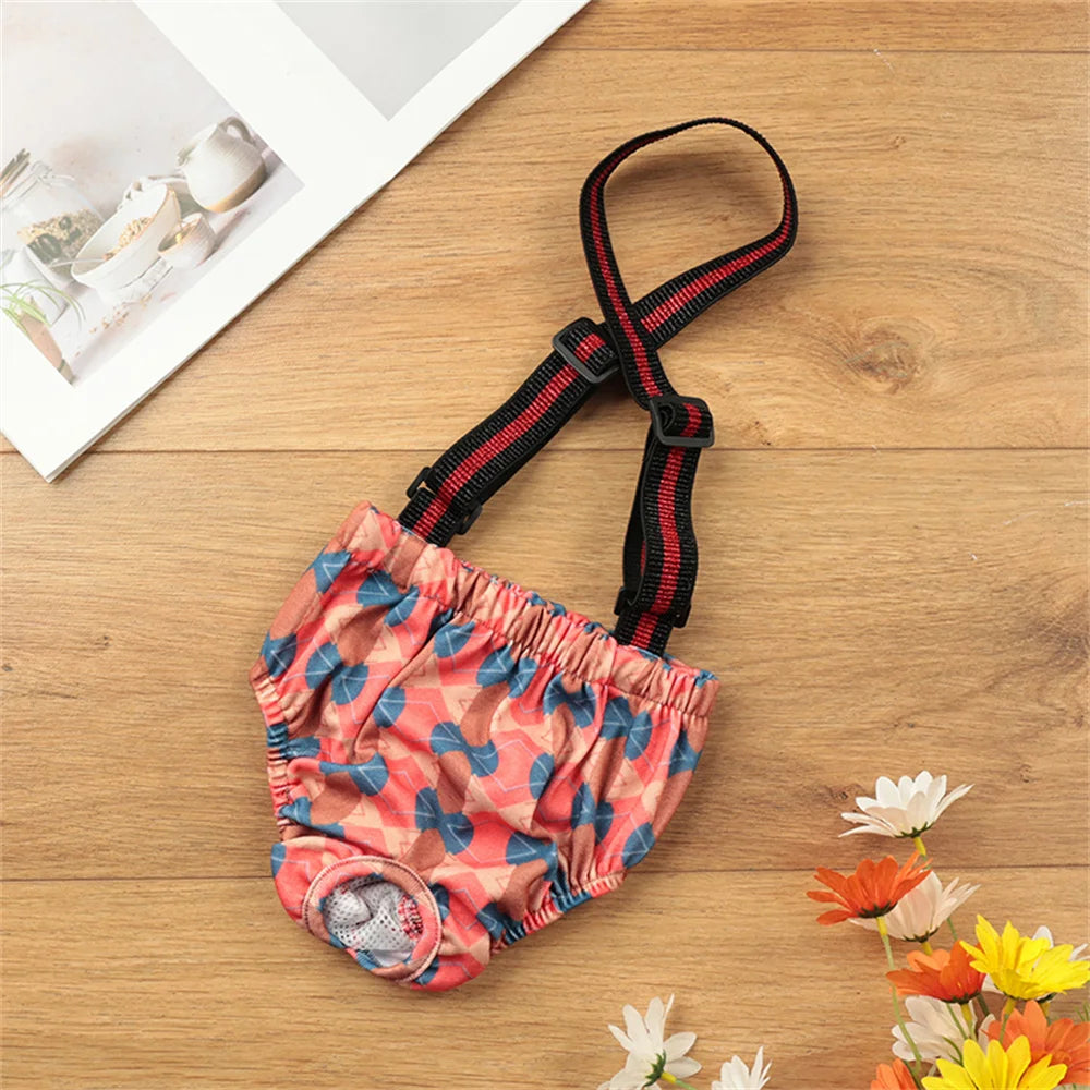 Ein Paar wiederverwendbare Hundschnallshorts in pink-orange gemustertem Stoff mit schwarzen Riemen, auf einer Holzoberfläche