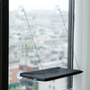 A black hanging hammock suspended by thin lines from suction cups, visible through a window overlooking a cityscape.