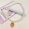 A delicate pearl necklace with a heart pendant displayed on a purple card.