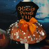 A black dress for a dog featuring gold lettering and an orange fabric with silver floral details and an orange bow.
