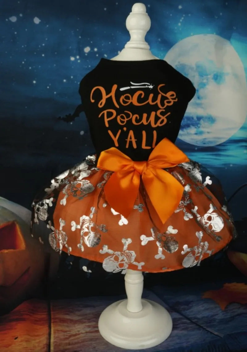 A black dress for a dog featuring gold lettering and an orange fabric with silver floral details and an orange bow.